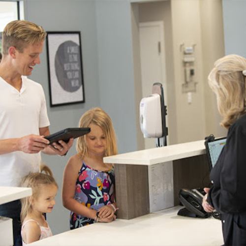 Father and his daughters checking in at dental office reception desk