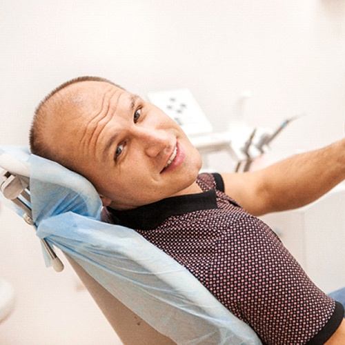 Man in polo shirt smiling with thumb up while sitting in dental chair