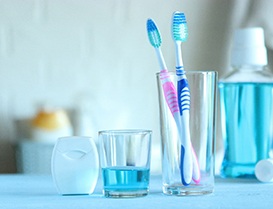 Toothbrushes, floss, and blue mouthwash sitting on countertop