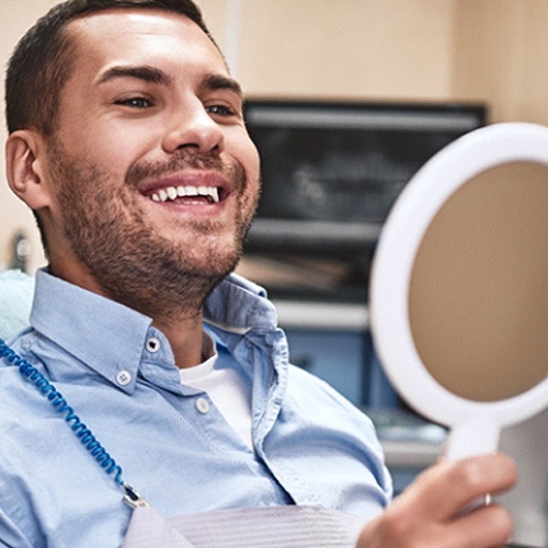 Man in dental chair smiling in handheld mirror