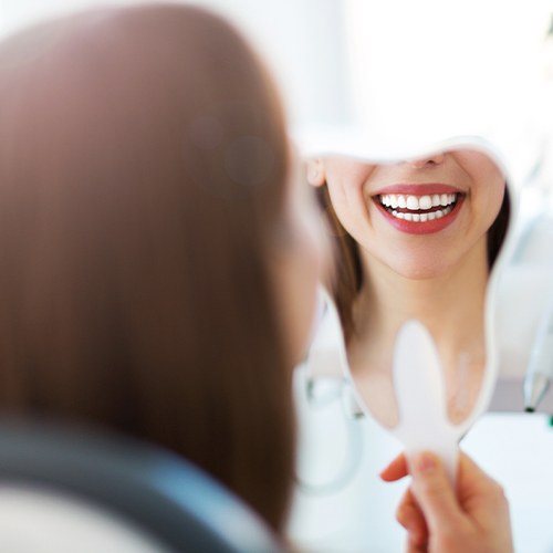 Woman looking at smile in mirror after smile makeover