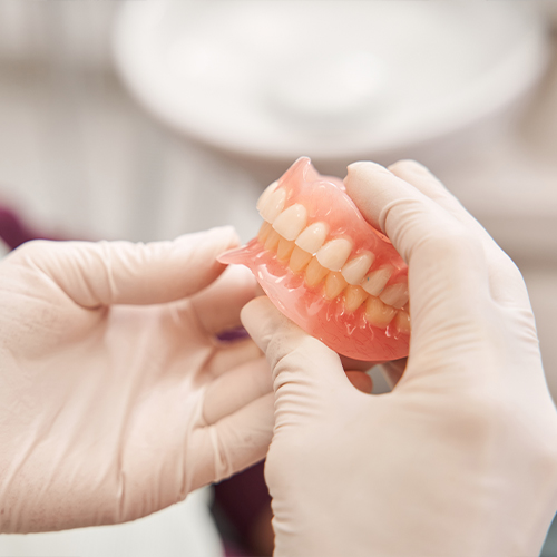 Gloved hands holding a set of full dentures