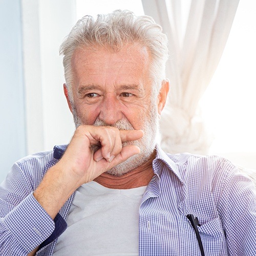 Older man in need of dentures covering his mouth