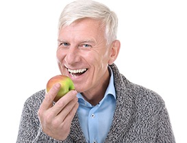 Older man in grey sweater biting into an apple