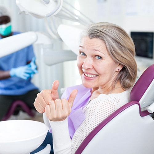 Woman smiling in dental chair with two thumbs up