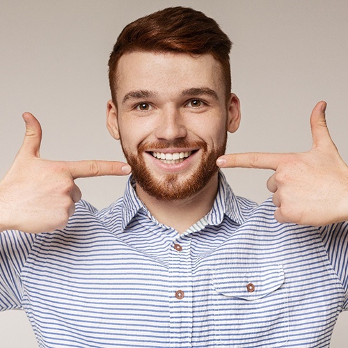 Man who cares well for dental implants, pointing at his smile