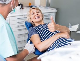 Woman giving thumbs up while sitting in the dental chair 