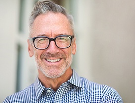 Man in plaid shirt smiling while wearing black glasses