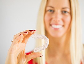 Woman in red shirt holding clear aligner with focus on clear aligner