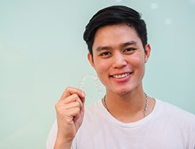 Man smiling while holding an Invisalign clear aligner