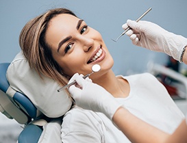 Woman smiling during her dental appointment with dentists hands near her