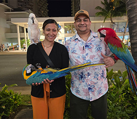 Doctor Dev smiling with tropical birds resting on their arms