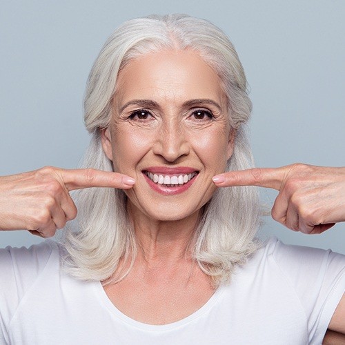 Woman with dentures pointing to her smile