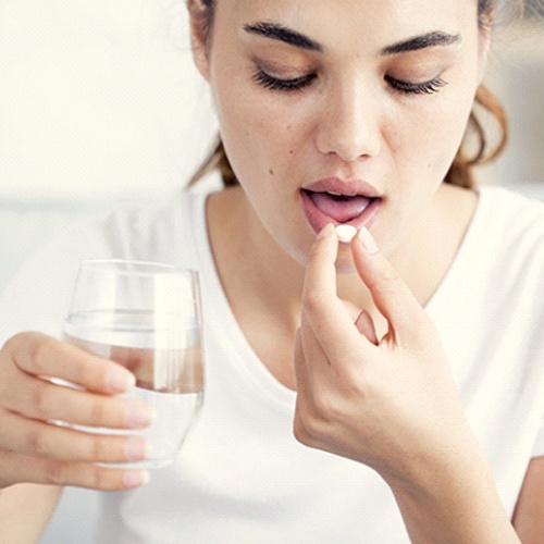 Woman holding a glass of water about to take a pill