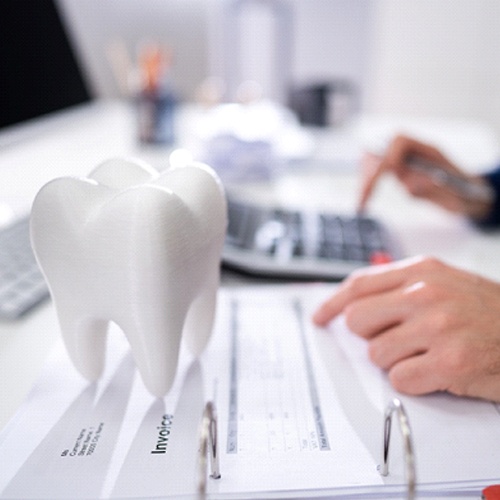 Person typing on calculator next to model of tooth