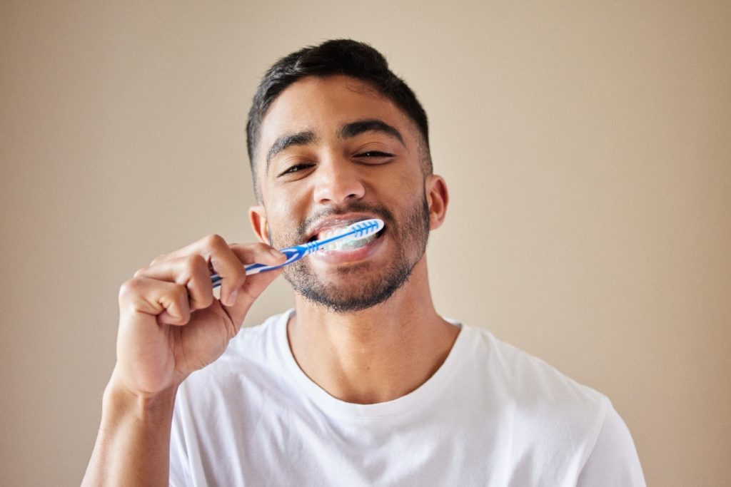 Man smiling while brushing his teeth