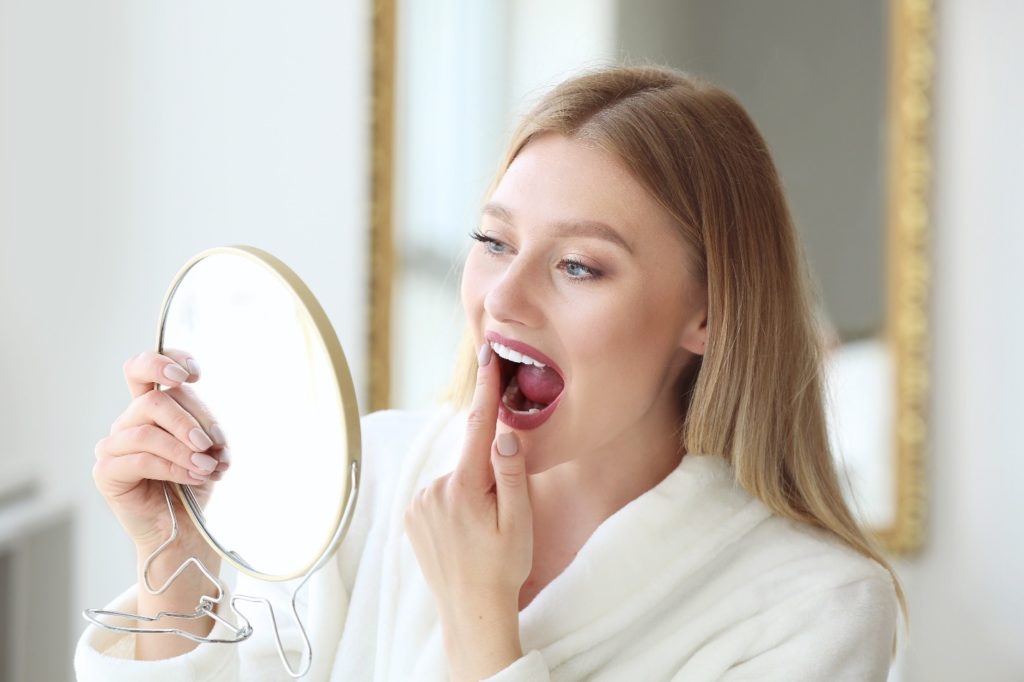 Woman in white robe looking at teeth in mirror