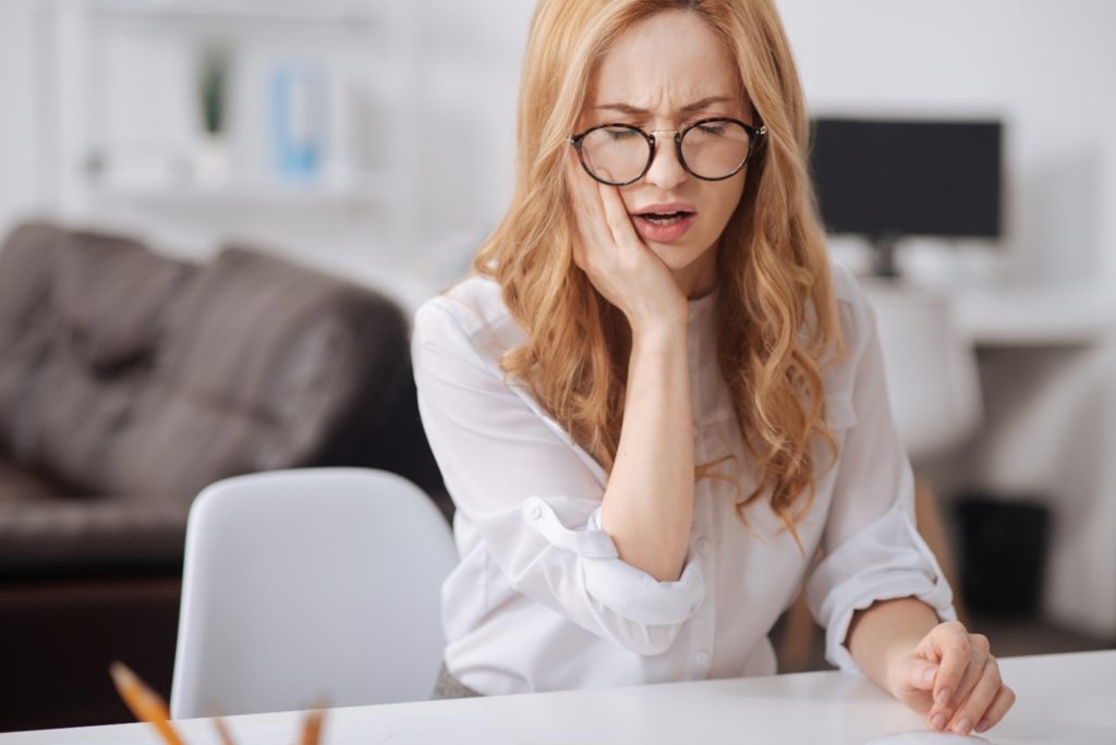 Woman struggling with tooth pain while working at desk