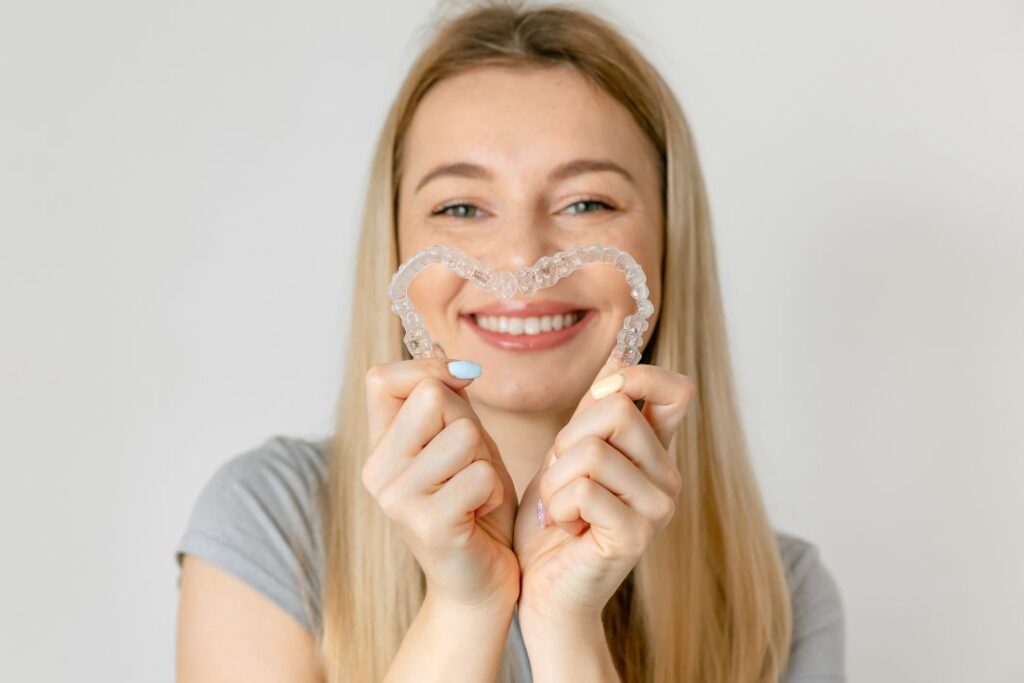 A woman making a heart with her Invisalign aligners
