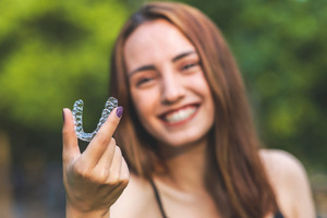 Woman holding Invisalign aligner and smiling